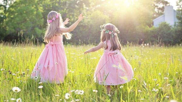 Zwei kleine Mädchen in rosa Kleidern auf grüner Blumenwiese im Tanz.