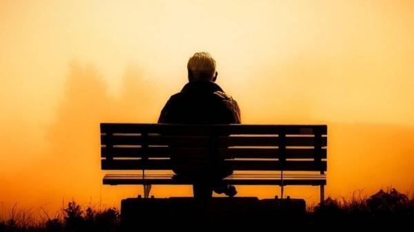 Rückseitige Ansicht eines alten Mannes auf einer Parkbank beim Sonnenuntergang.