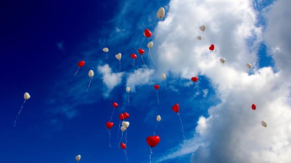 Weiße und rote Luftballonherzen vor einem blauen Wolkenhimmel austeigend.