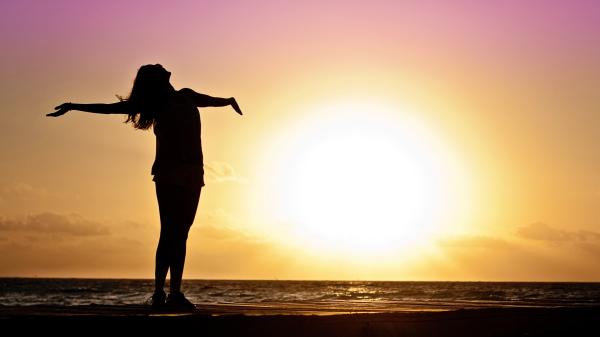 Eine Weibliche begrüßt die aufgehende Sonne am Meer.