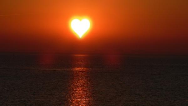 Sonne in Herzform über dem Meer.